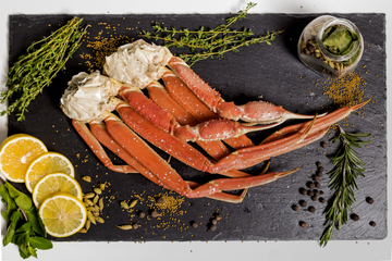 A cluster of snow crab legs along with lemon slices and herbs on a slate serving board. 