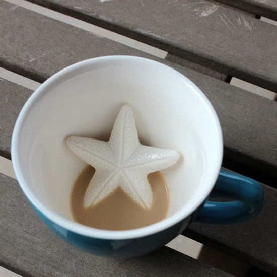 A blue coffee cup with a 3D starfish design, with a portion of the cup filled with a brown beverage.