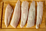 Several cleaned flounder fillets arranged on a wooden cutting board. thumbnail