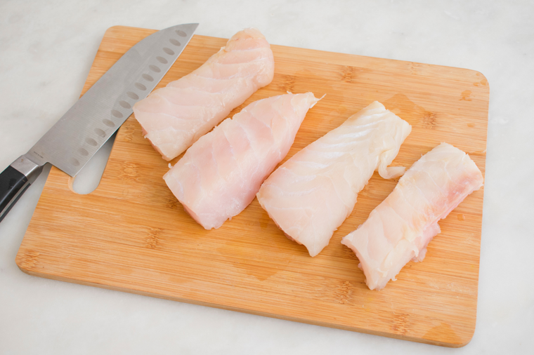 Four Grouper fillet pieces with knife on top of cutting board