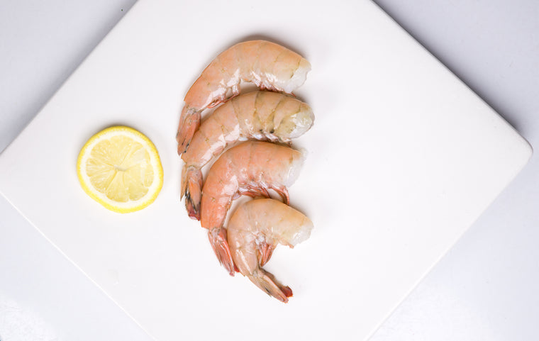 Four headless shrimp with lemon on top of white plate