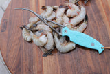 Shrimp deveiner laying on top of headless white shrimp thumbnail