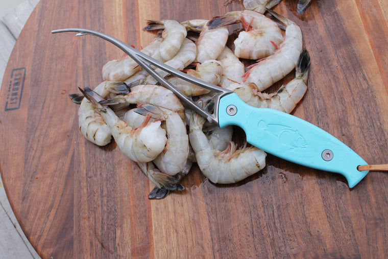 Shrimp deveiner laying on top of headless white shrimp