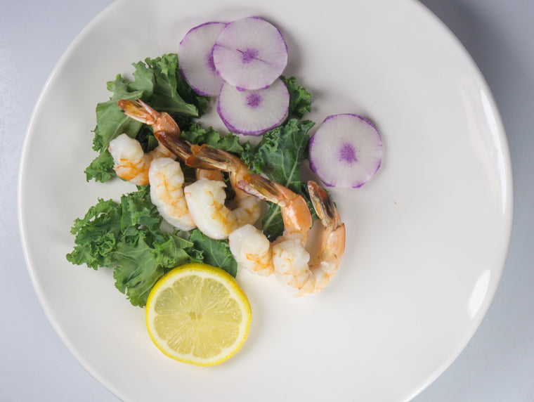 Peeled brown shrimp on top of kale with side of lemon and radish