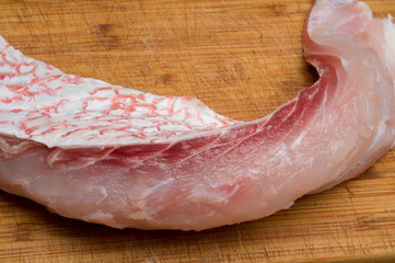 A piece of fresh red snapper on a wooden cutting board. 
