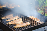 Smoked mullet fish on a grill, being smoked over wood chips with smoke rising. thumbnail