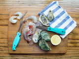 Peeled shrimp, headless shrimp, oysters, lemon, tea towel and shrimp deveiner laying on a wood cutting board thumbnail