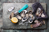 Oysters, oyster knife, tea towel and lemon laying on stone board thumbnail