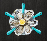 Shucked oysters and oyster knives in star pattern on top of white dish with lemon in the middle thumbnail