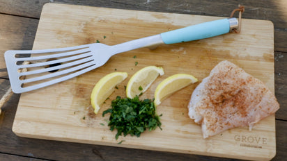 Fish spatula, parsley, lemon slices and fish fillet laying on wood cutting board 